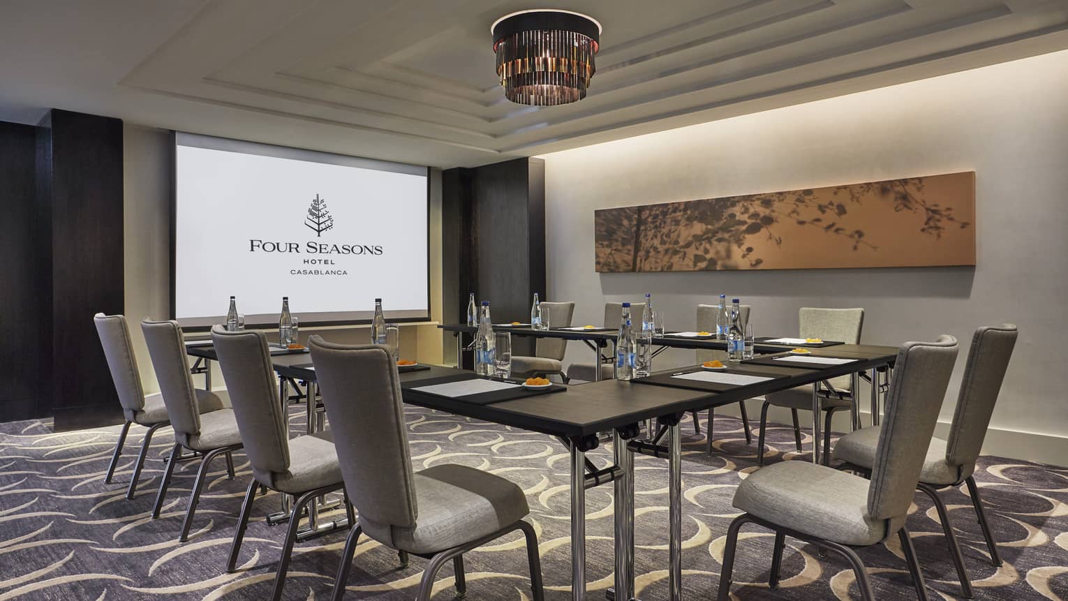 Business meeting room with large screen with Four Seasons logo, tables and chairs