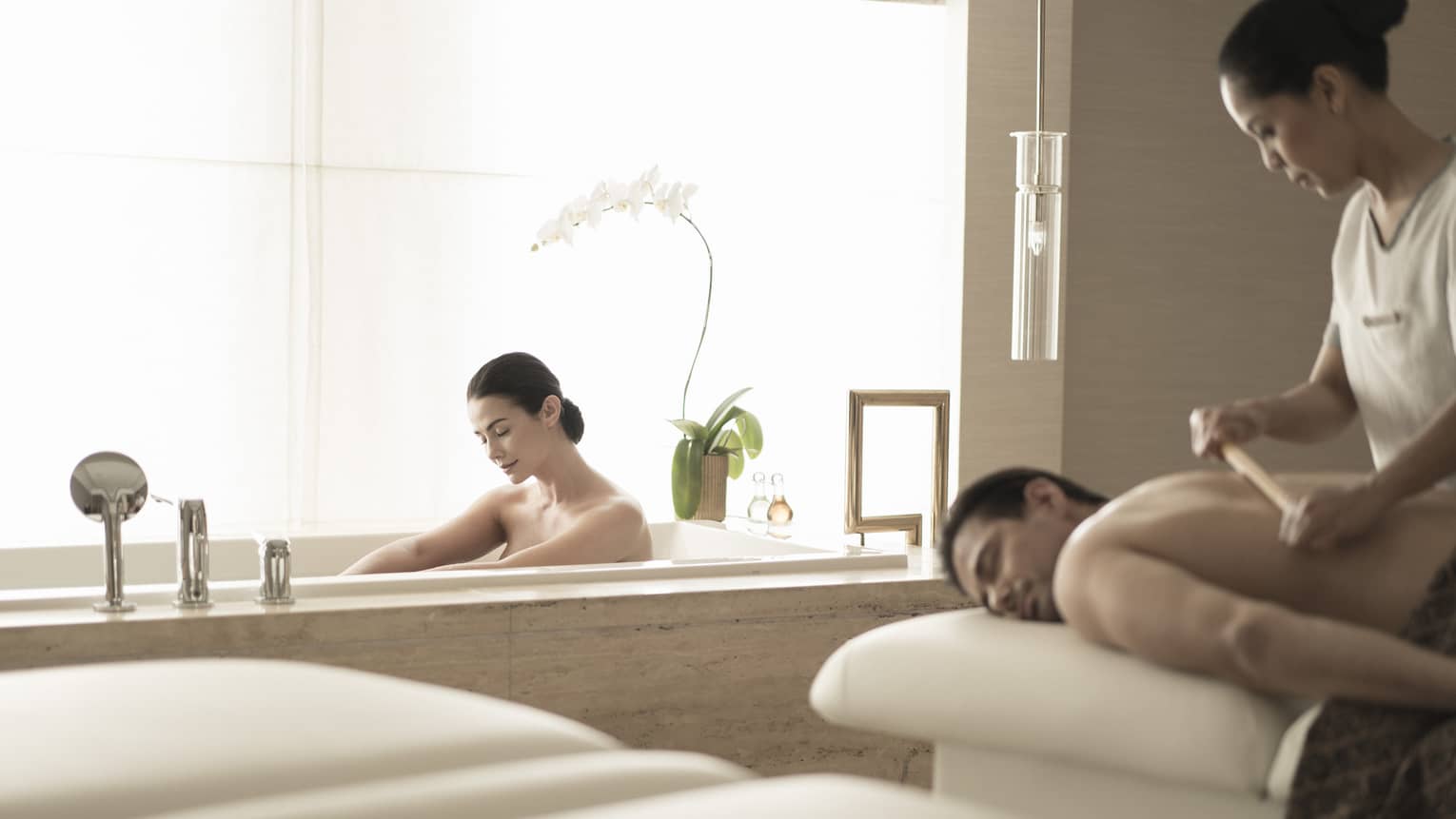 Woman soaks in spa tub near man getting massage 