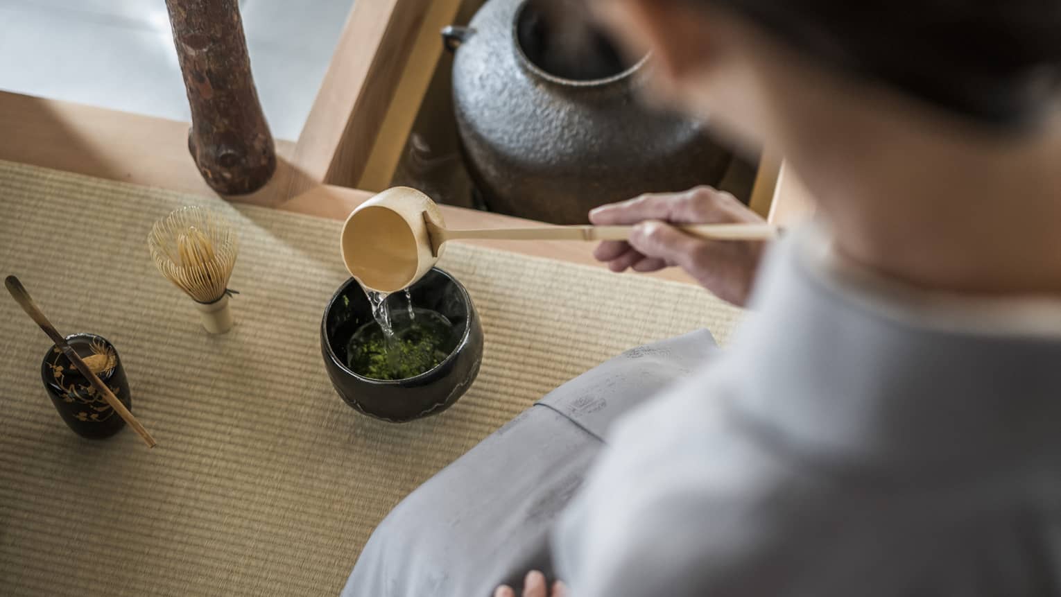 Woman kneels and pours tea from ladle during Tea Ceremony