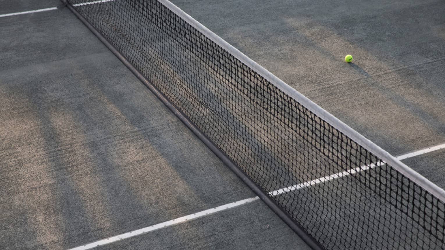A lone tennis ball lies near the net on an empty court