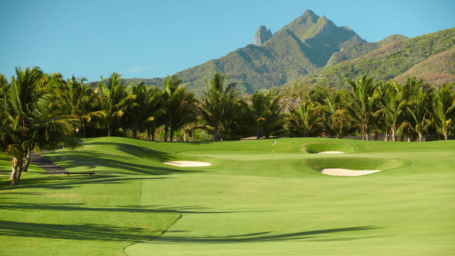 Fifteenth hole rolling golf course green dotted by two sand traps, mountain backdrop