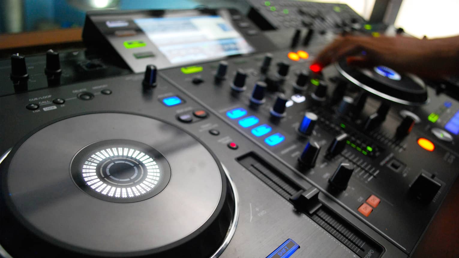 Close-up of DJ console discs, buttons, lights, hand adjusting levels