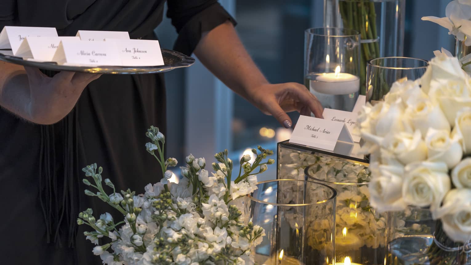 Event staff with tray places name cards on elegant banquet table with white flowers, candles