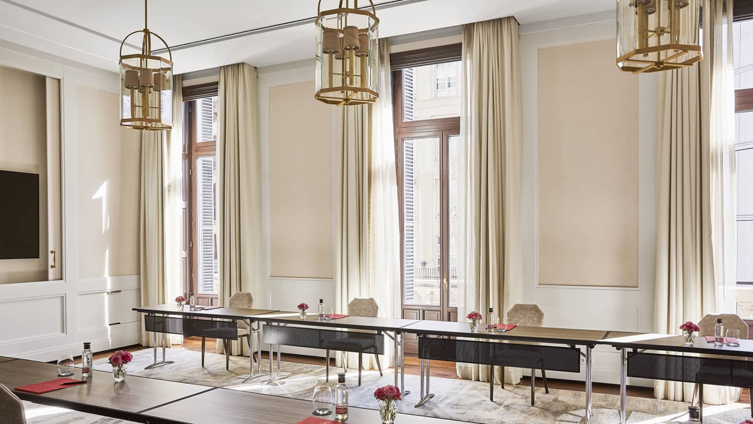 Meeting room with u-shape table set-up, three small chandeliers hanging from ceiling, three windows