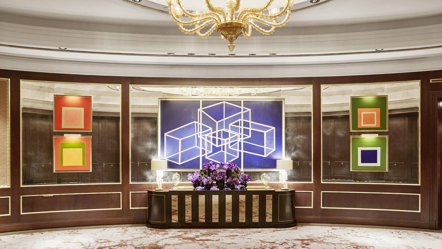 Sol Foyer with mirrored walls, colourful artwork, centre table with purple flowers, gold chandelier