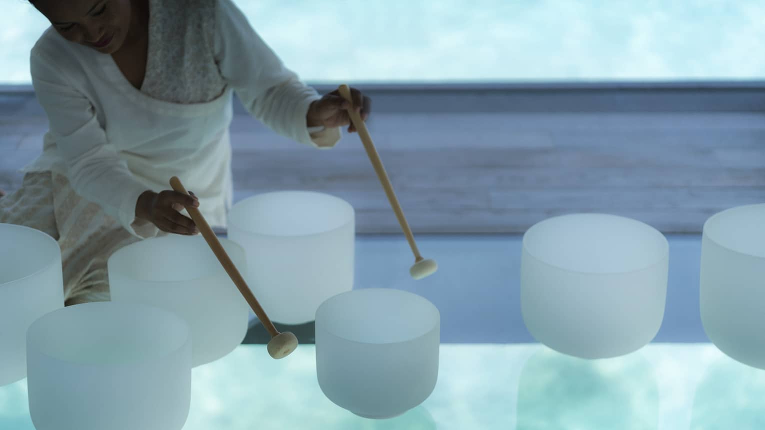 Spa staff plays various white crystal bowls with wood mallets during sound healing session