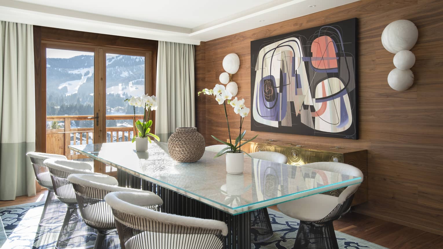 Wood-panelled dining room with modern art, rectangular glass table and round metal chairs, and mountain views