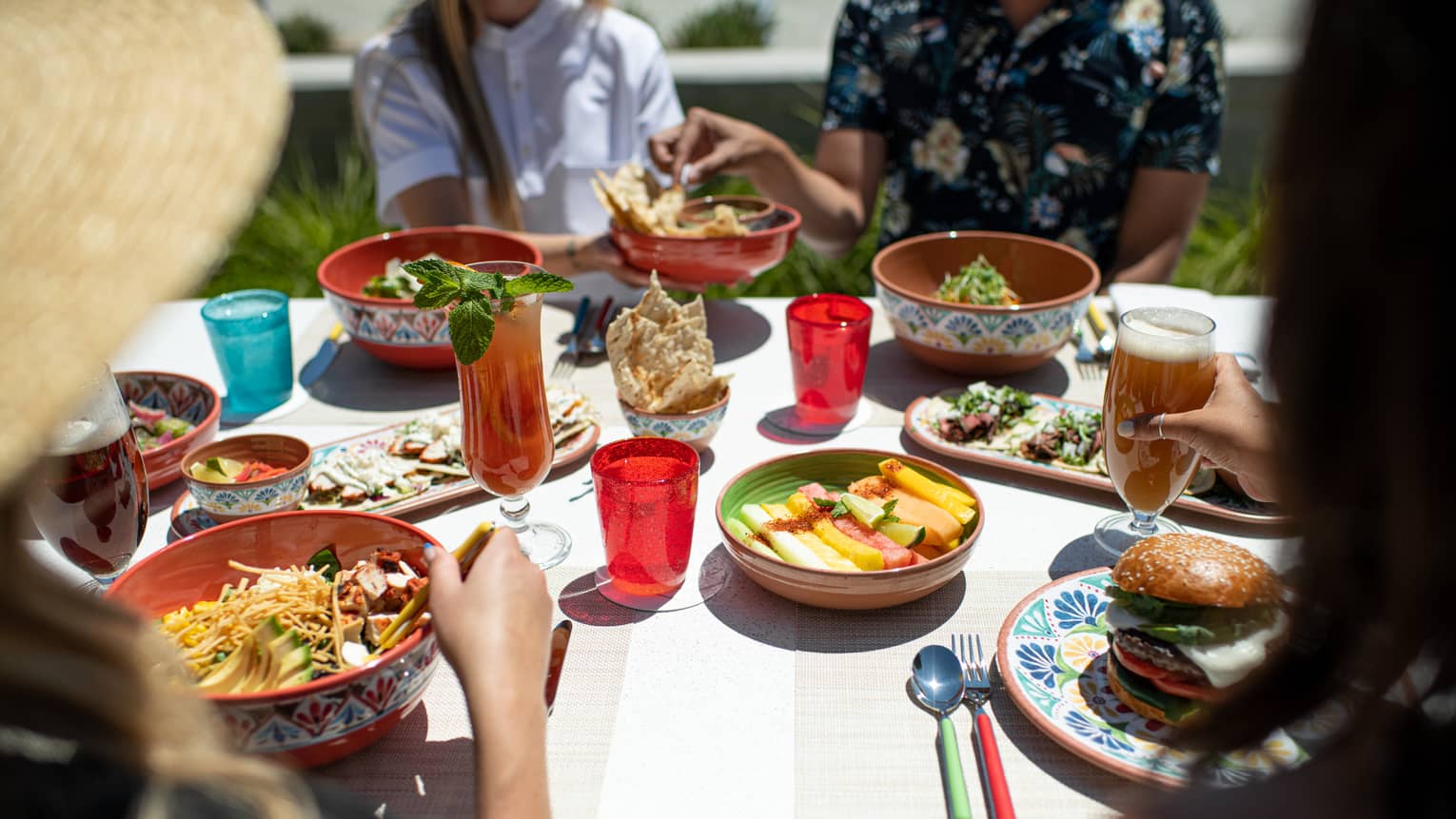 A group of young people eating food outside on colourful plates and bowls.