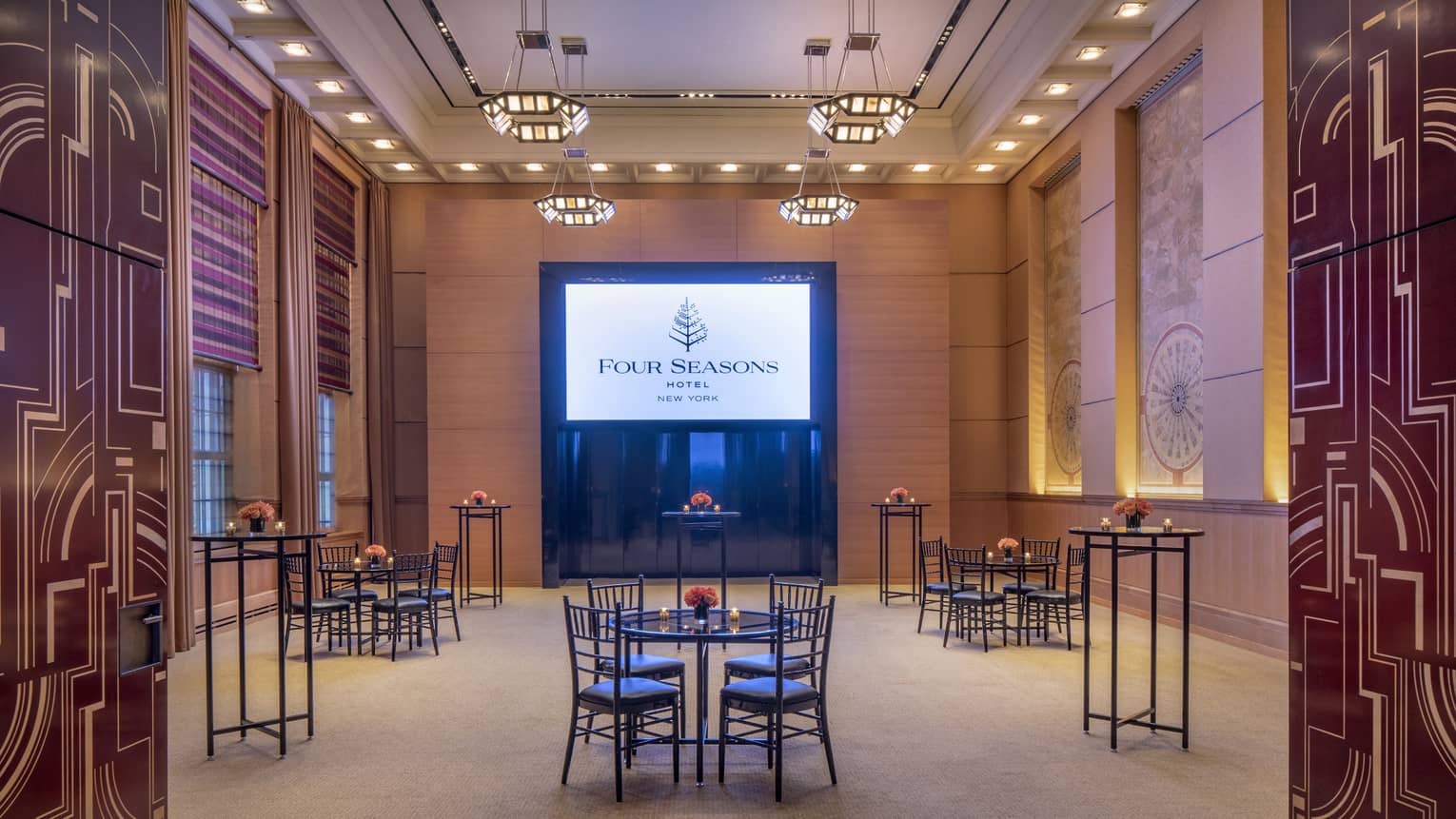 Orante and abstract lines decorate two doors that are opened to reveal a wood-panelled function room with three small black iron tables and chairs facing a presentation screen that shows a slide with the four seasons logo
