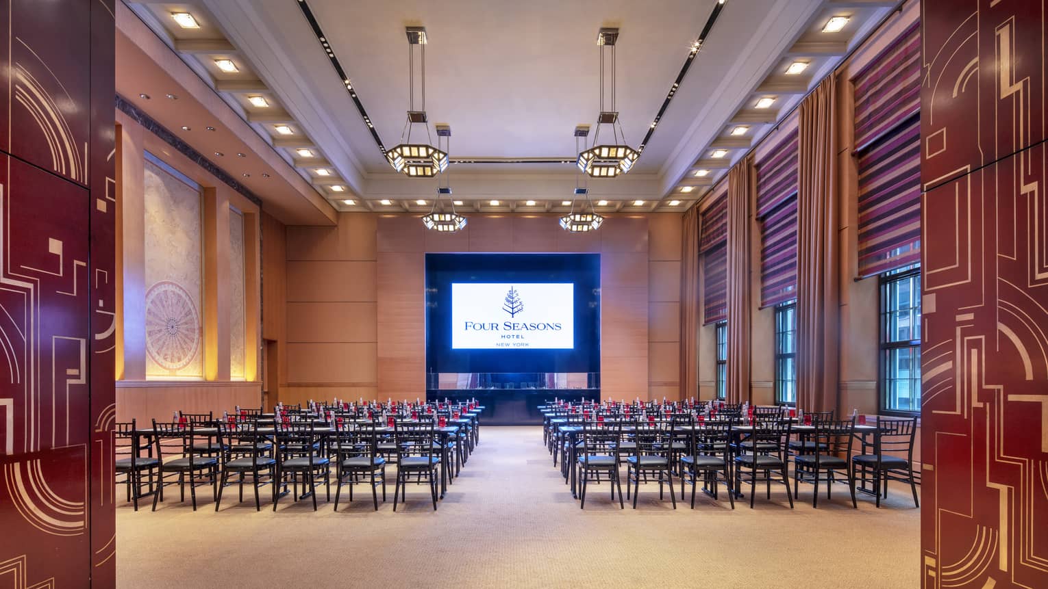 red and gold abstract lines decorate two doors that are opened to reveal a wood-panelled function room with rows of chairs facing a presentation screen