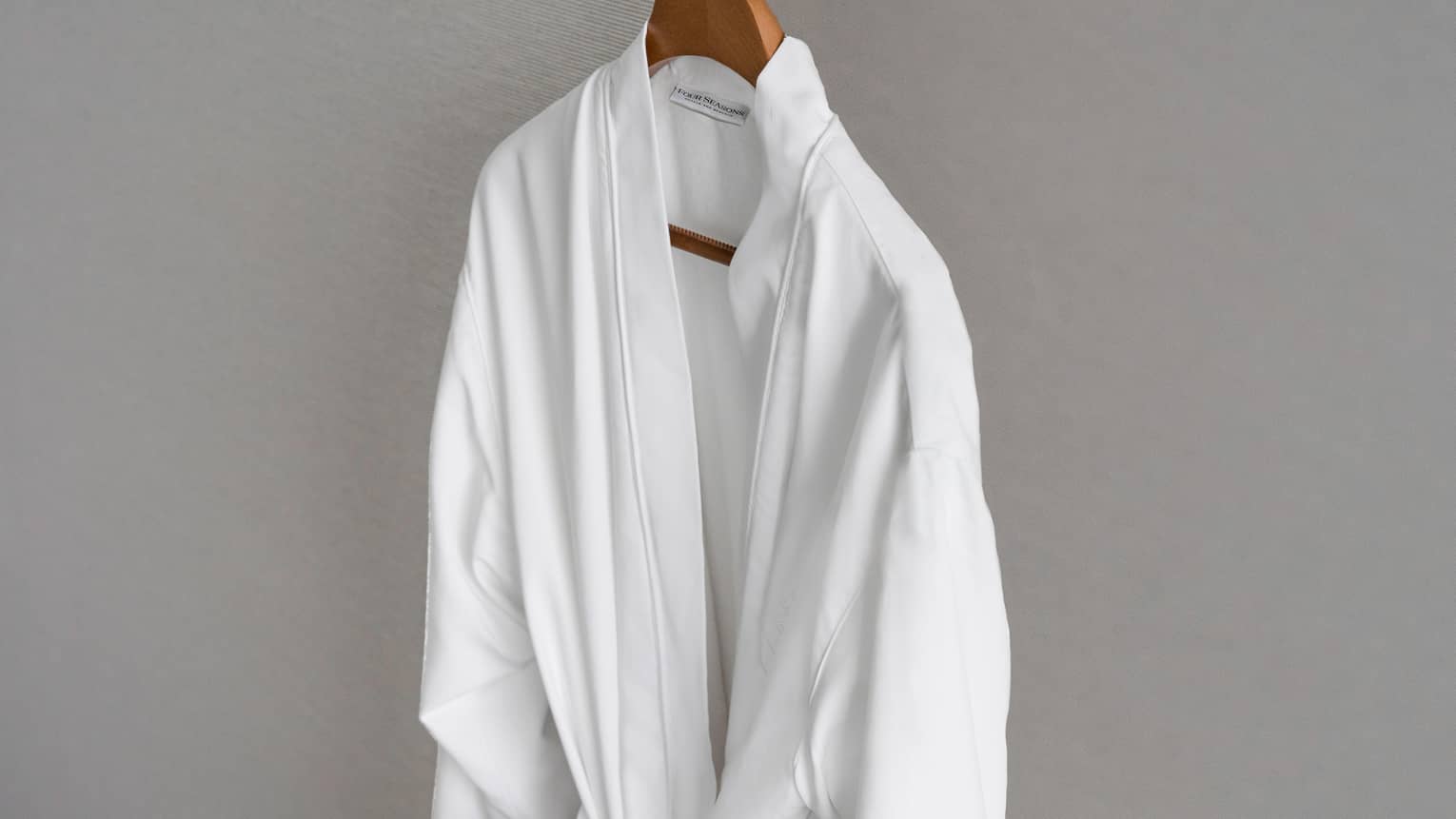 Four Seasons white bathrobe hanging on wooden hanger
