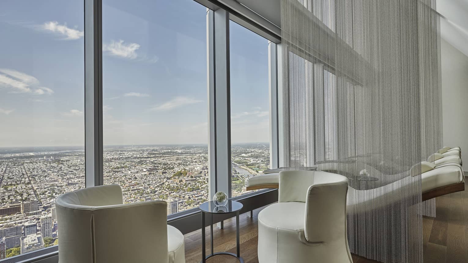 Lounge with two beige chairs and windows overlooking the city.