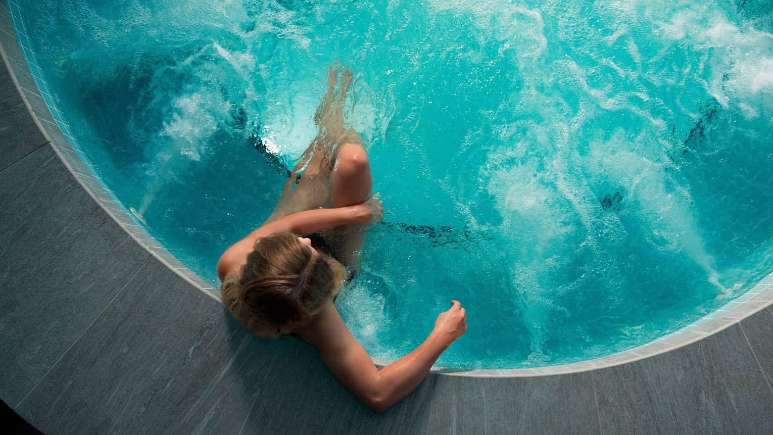 Looking down at woman sitting in round hot tub with blue water