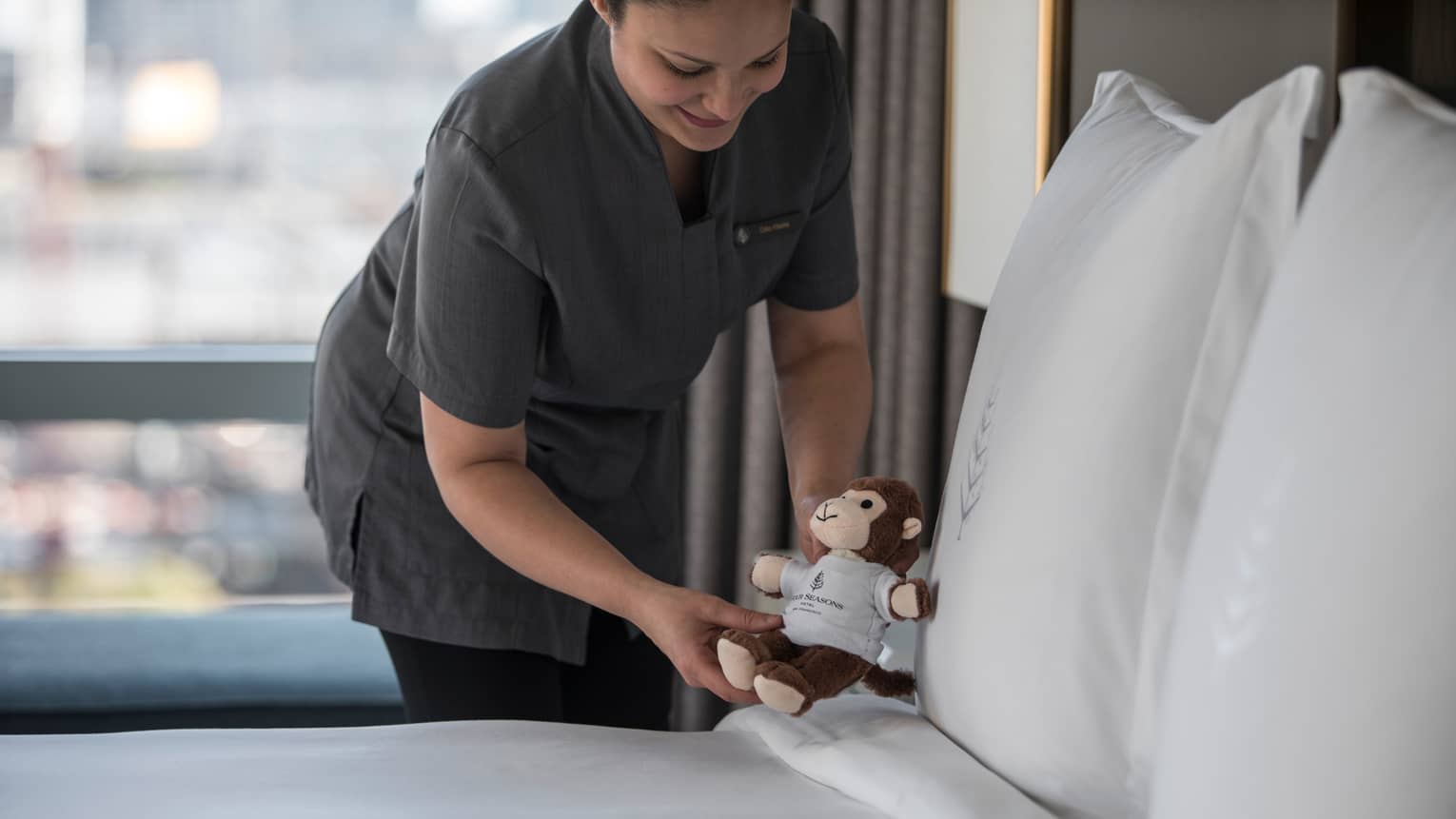 Hotel staff sets small stuffed monkey toy down on made hotel bed