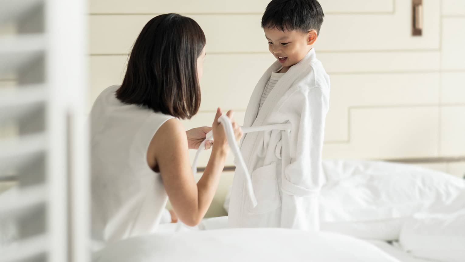 Woman kneels in front of young child, ties front of his white bathrobe