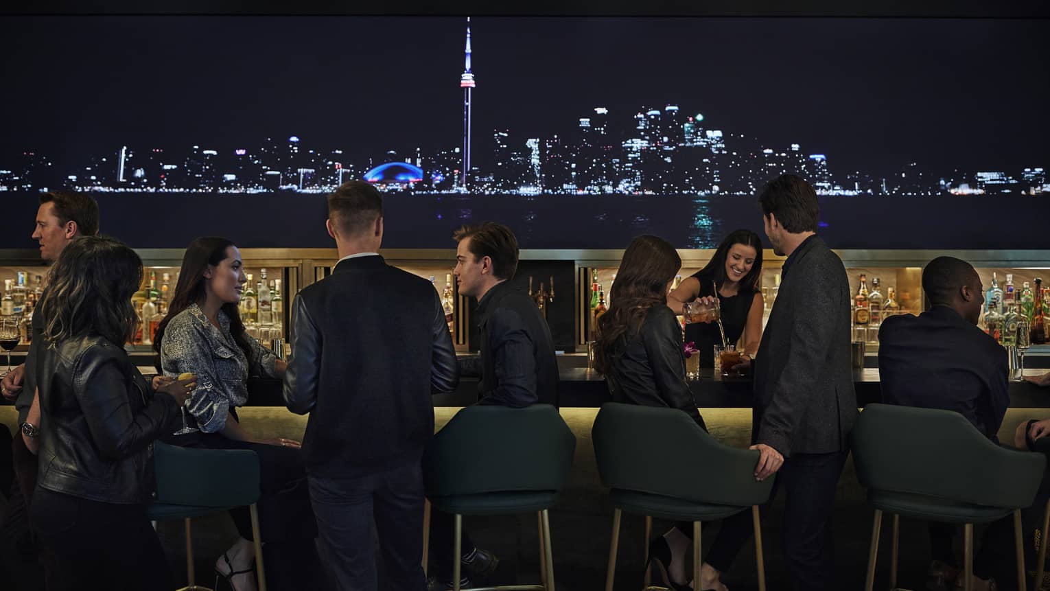 A lit up skyline of the city illuminate the bar, where guests sit and enjoy drinks