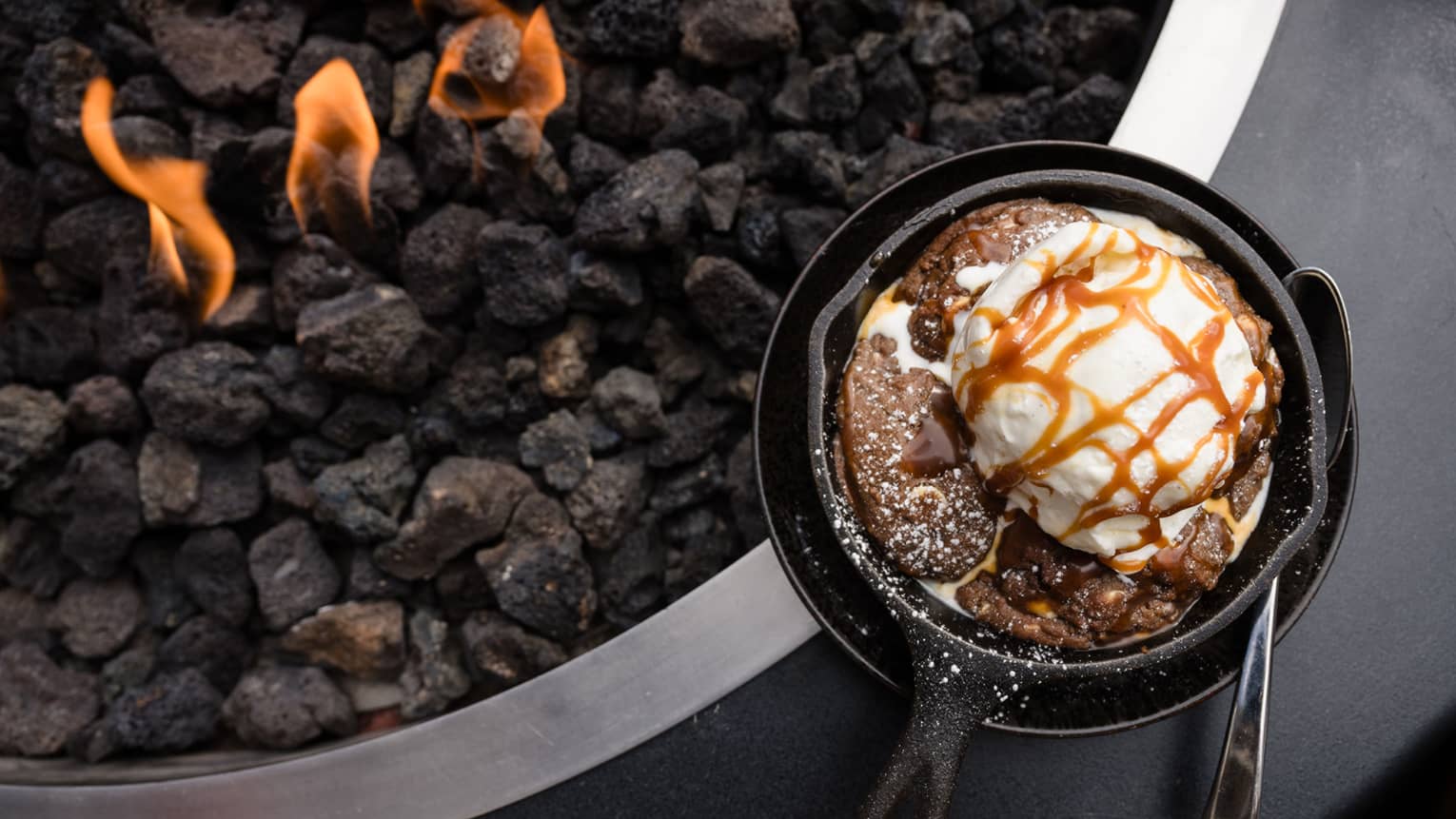Ice cream in a pan next to a charcoal grill.