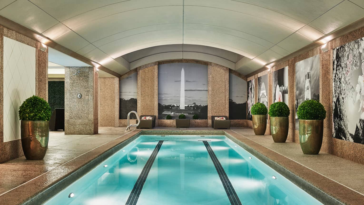 Long indoor lap swimming pool, large gold planters on deck, wall with black-and-white mural of the Washington Monument