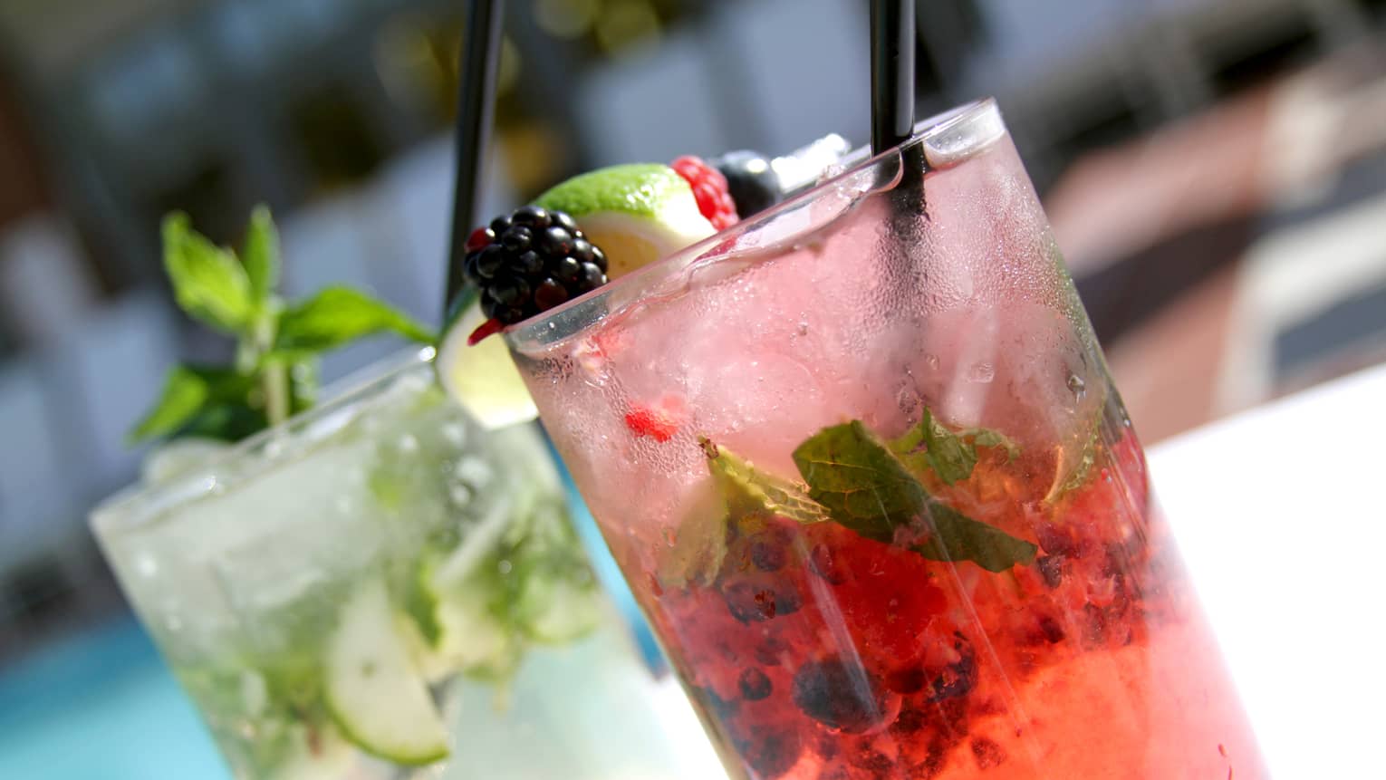 Two different mojitos: one pink garnished with fruit, one with cucumber and mint