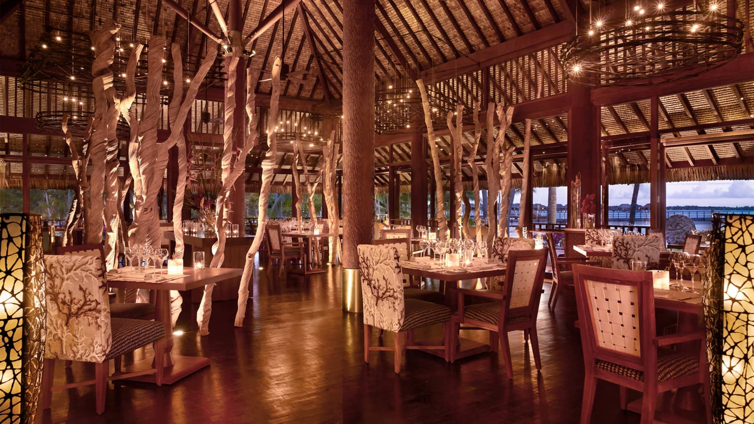 Elegant, candle-lit Arii Moana open-air dining room with plush chairs, decorative branches 