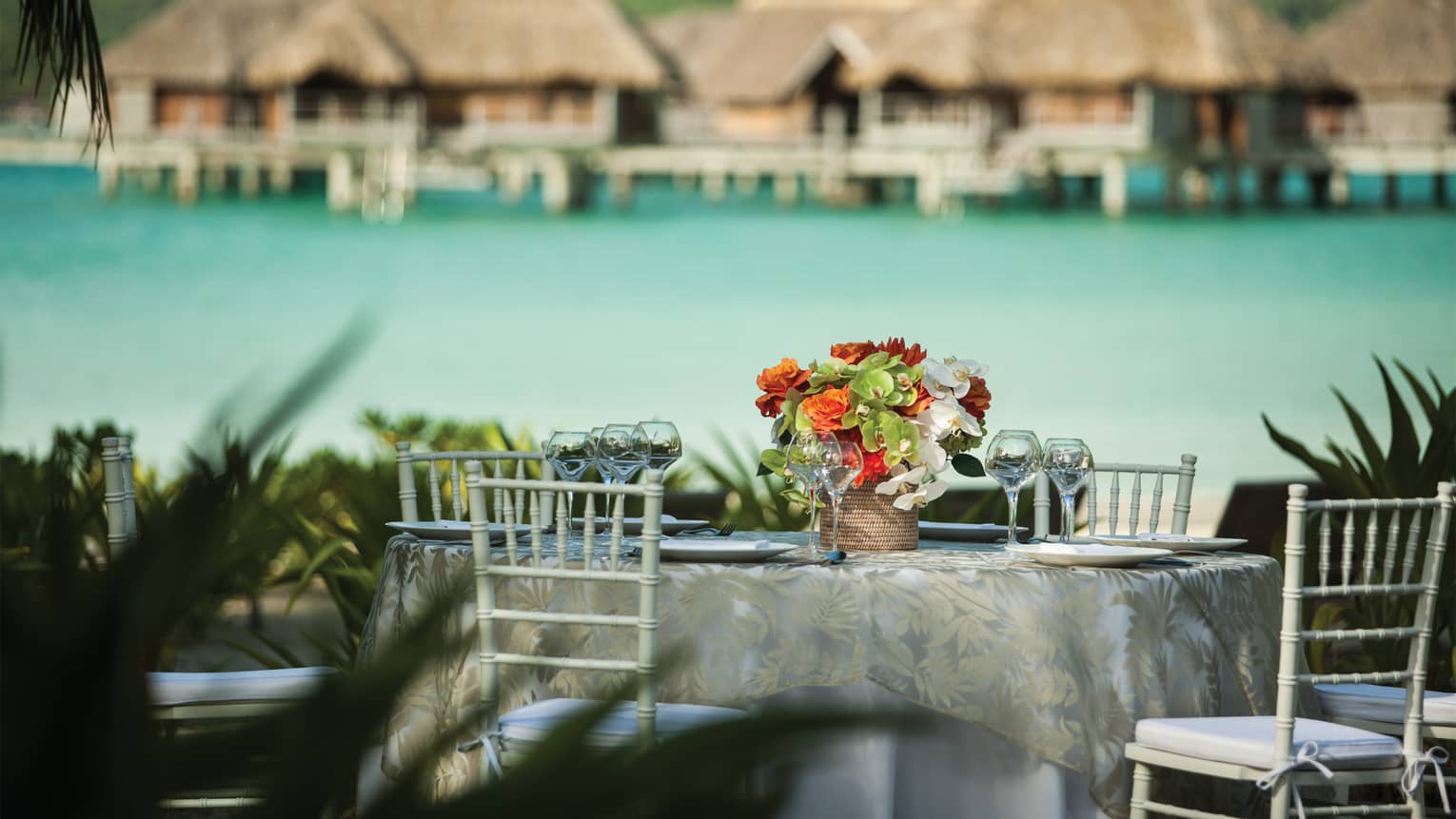 Outdoor formal dining table with fresh flower arrangement, ocean and overwater bungalows in background