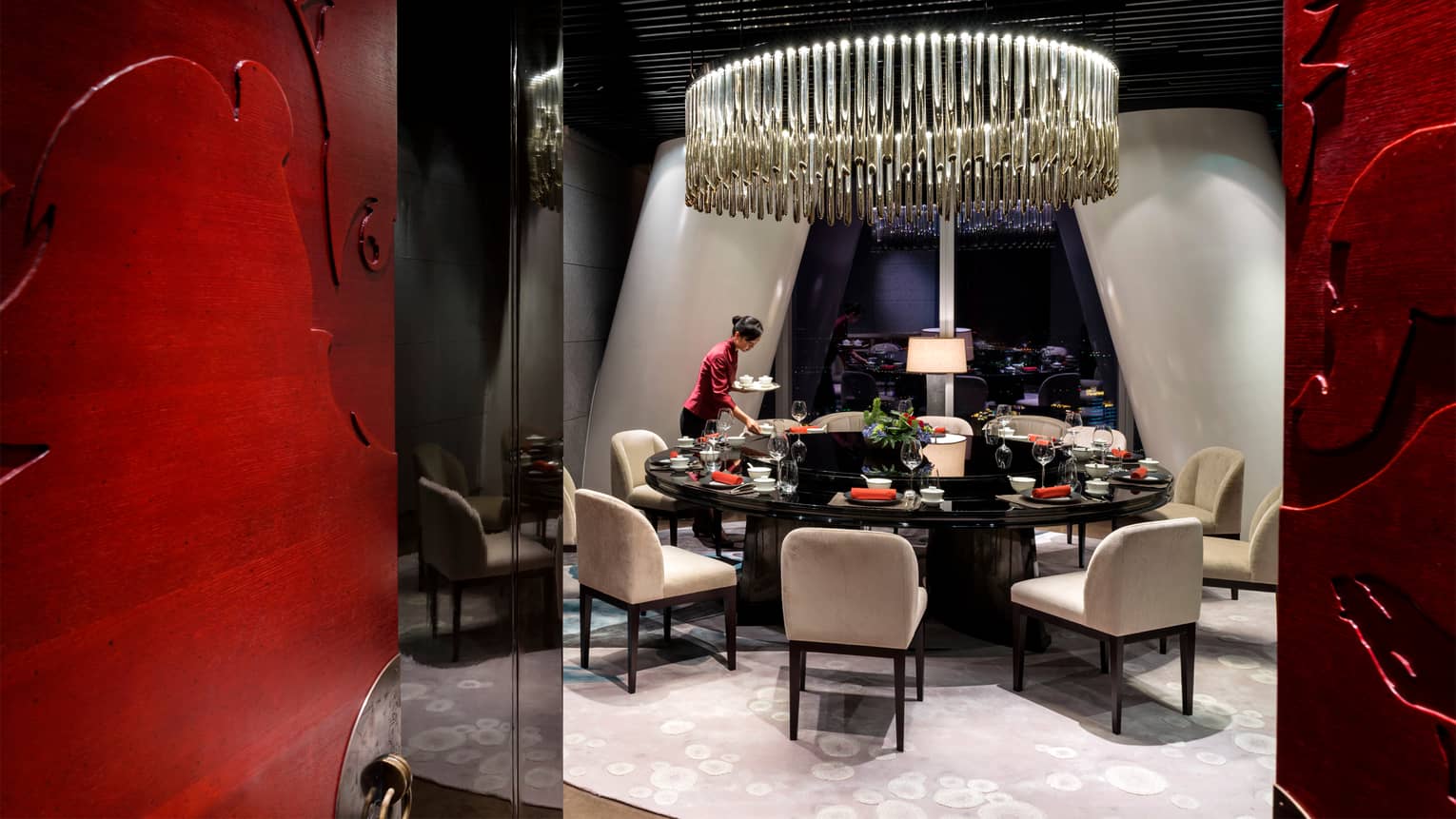Yu Yue Heen server in red shirt sets round formal private dining table under large chandelier 