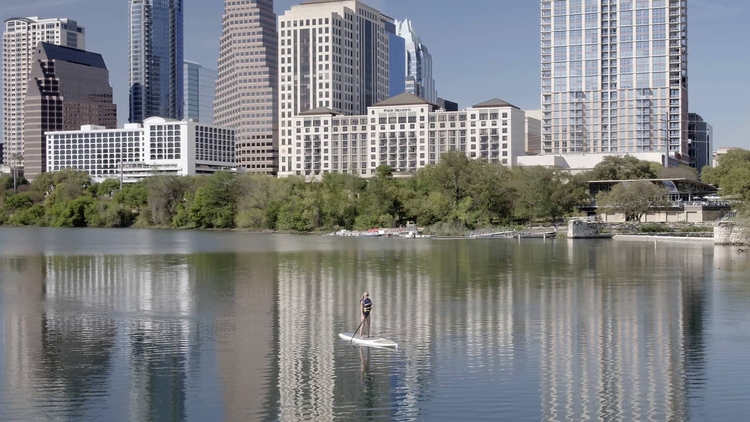 Person stand up paddleboarding on lake, Austin city skyline in background