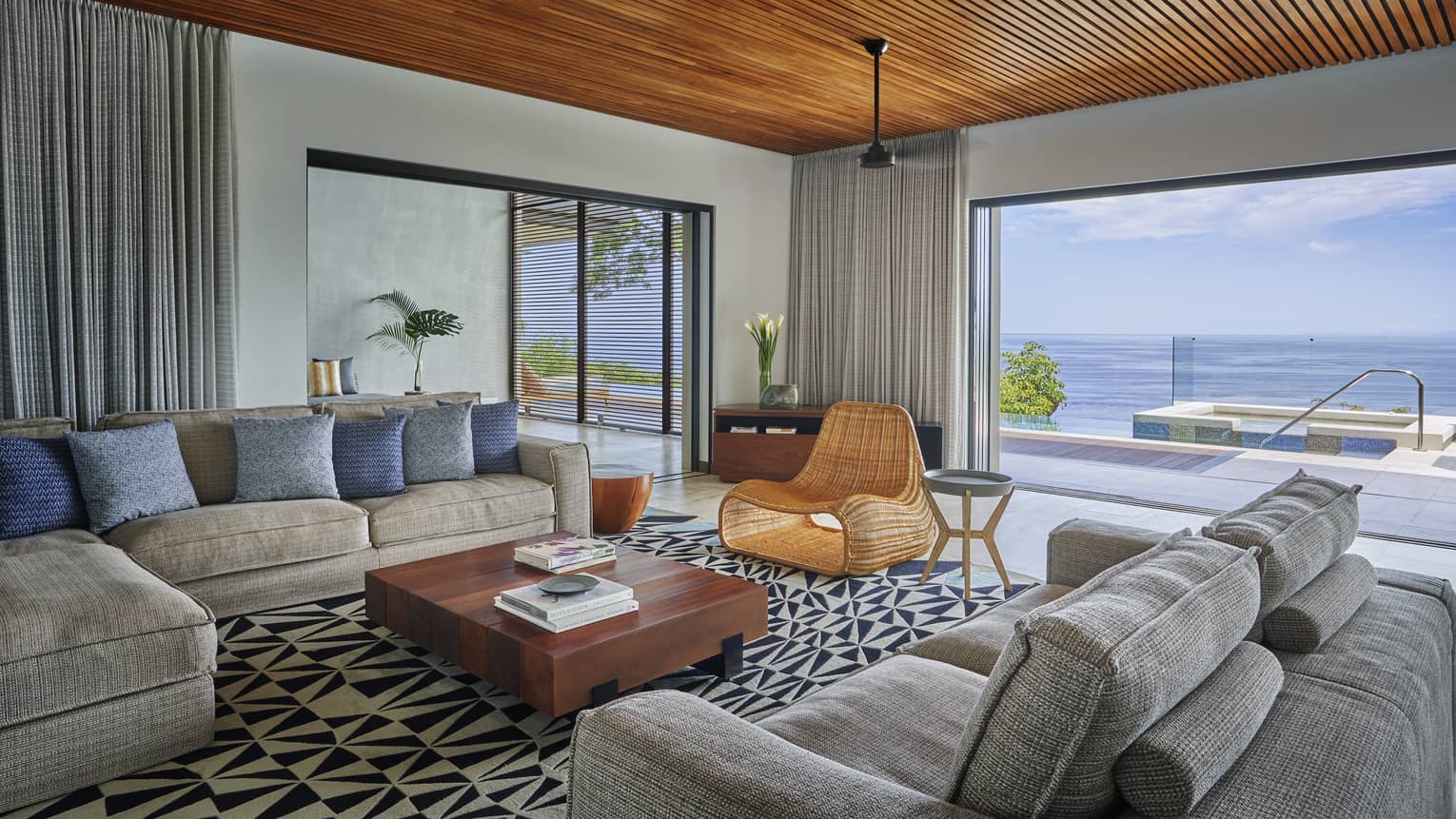 Living room with two grey sofas, whicker chair, opening to pool deck and sea view