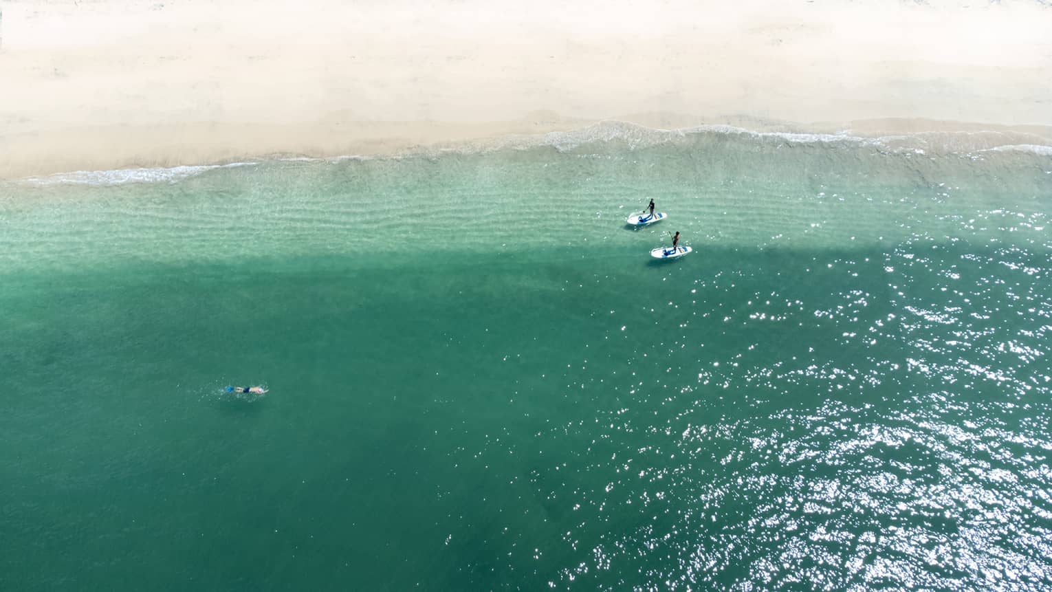 Distant aerial view of two people riding stand-up paddleboards near the shoreline