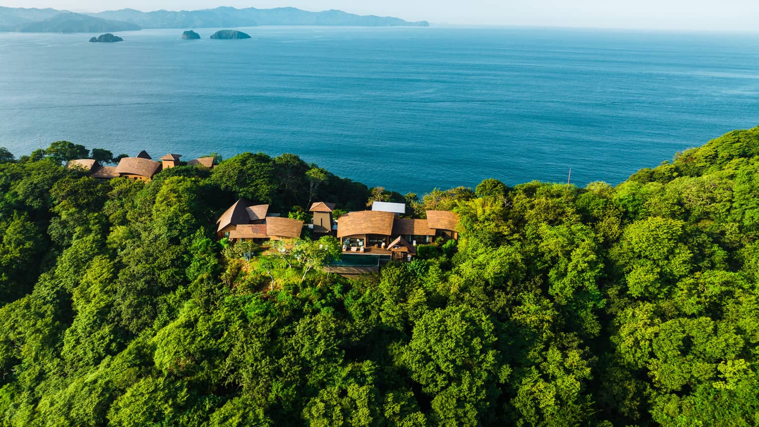 Aerial view of expansive private residence nestled in the jungle and overlooking the blue ocean waters