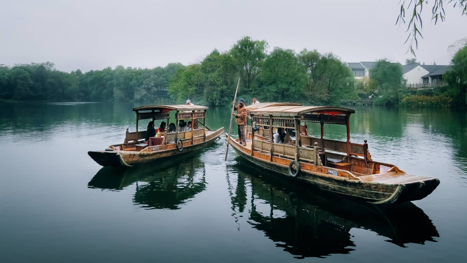People dine on Chinese wooden rowboat next to boat where man steers with paddle on West Lake