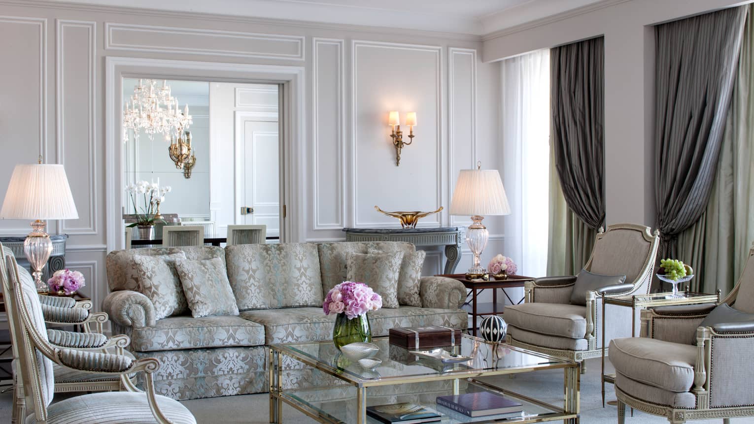 Royal Suite bright, elegant living room with blue-and-grey satin sofa, armchairs, glass coffee table with gold trim, white walls