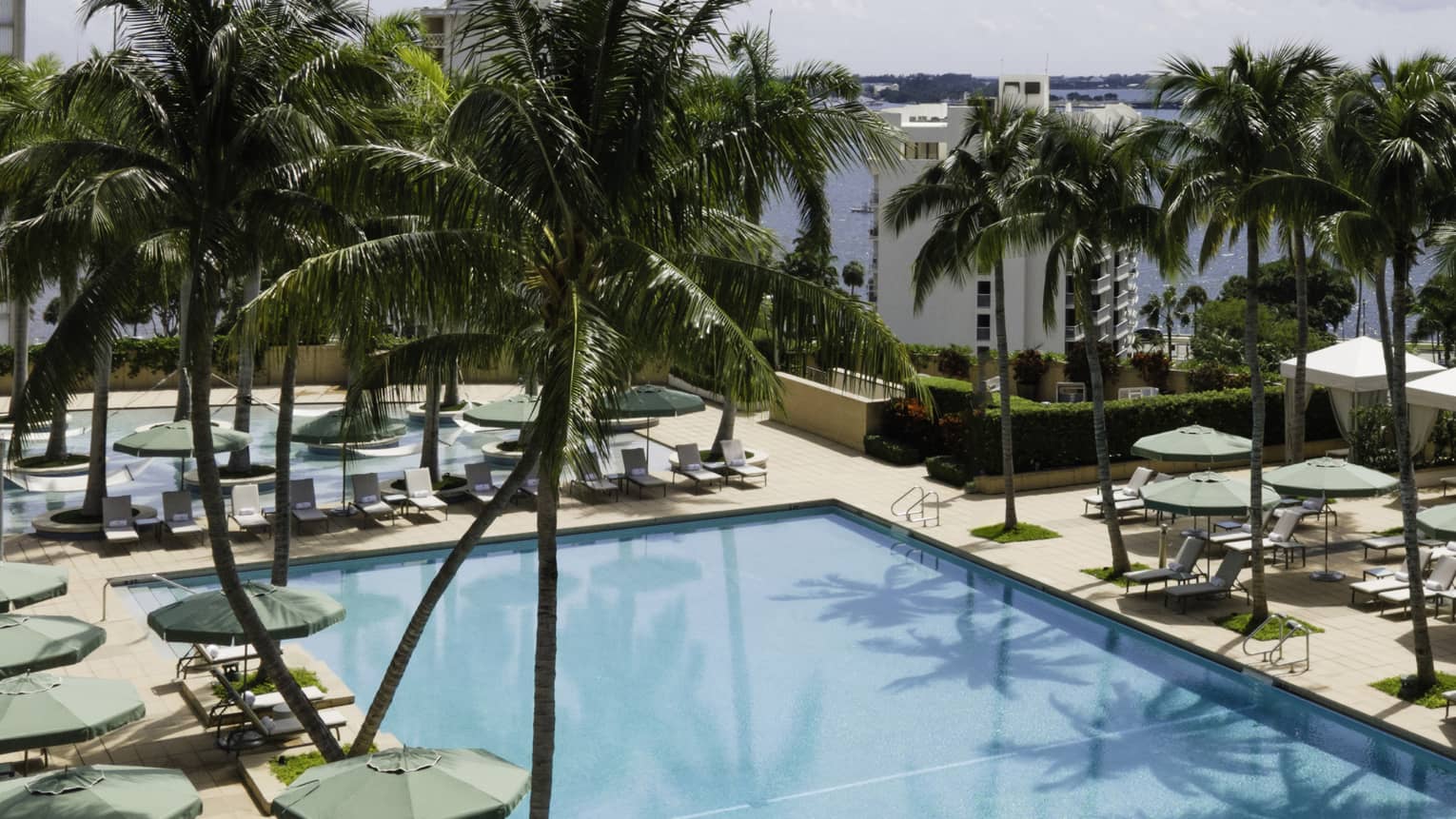 Pool with green umbrellas, lounge chairs and palm trees.