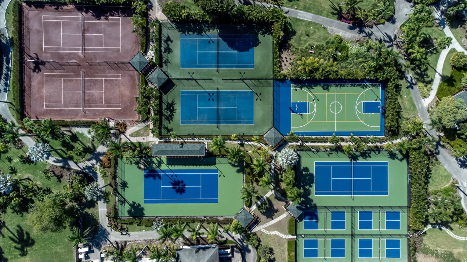 An aerial view of different tennis and pickleball courts surrounded by trees.
