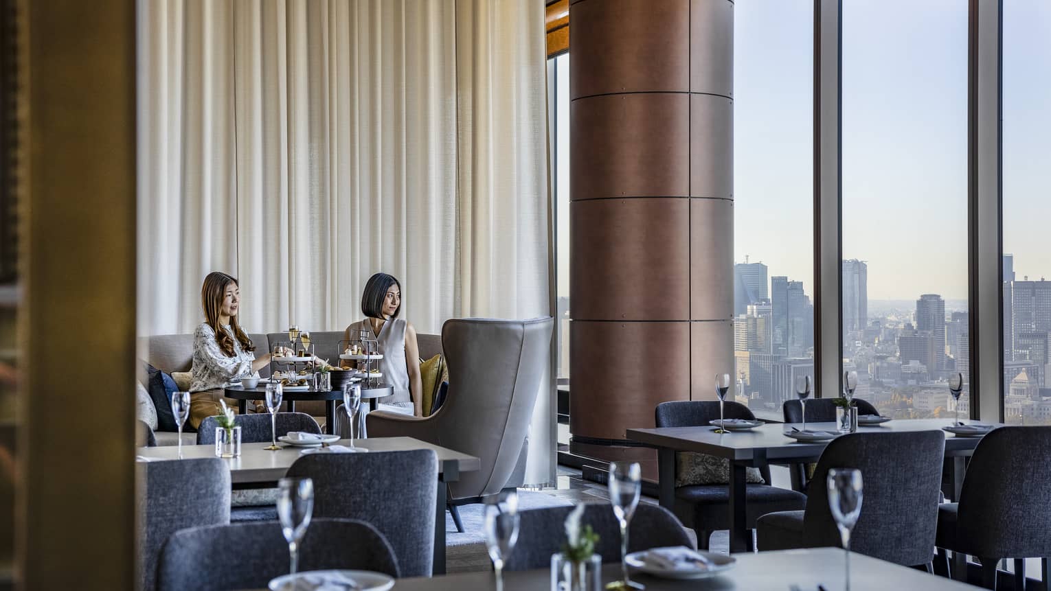 Two female guests enjoy Afternoon Tea at The Lounge as they gaze out the floor-to-ceiling windows at the Tokyo skyline