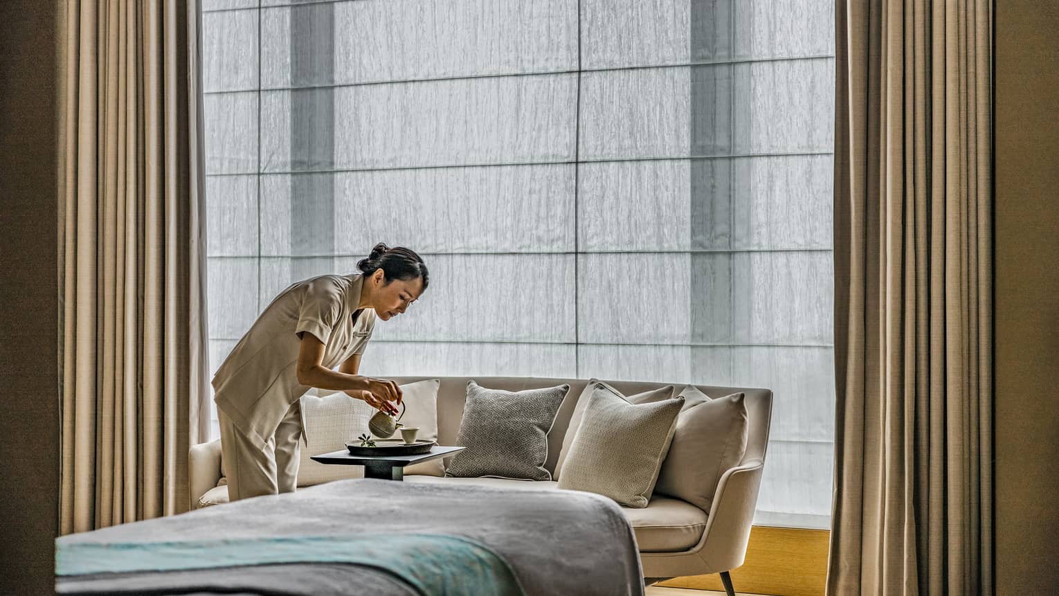 Spa team member pours hot tea into a cup, a cream couch and treatment table in the background 