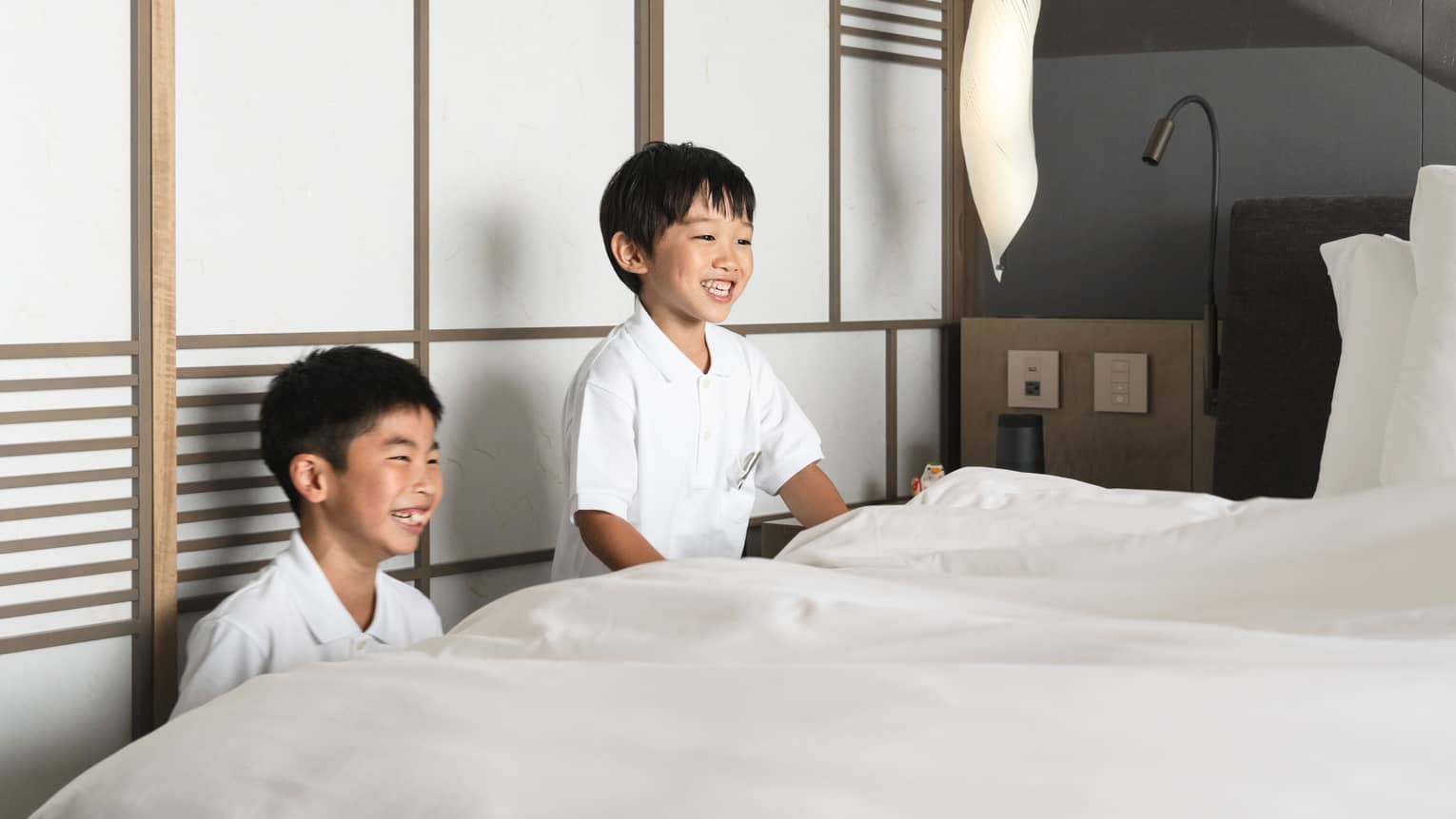 Two laughing boys straighten the linens on a bed at Kids Academy