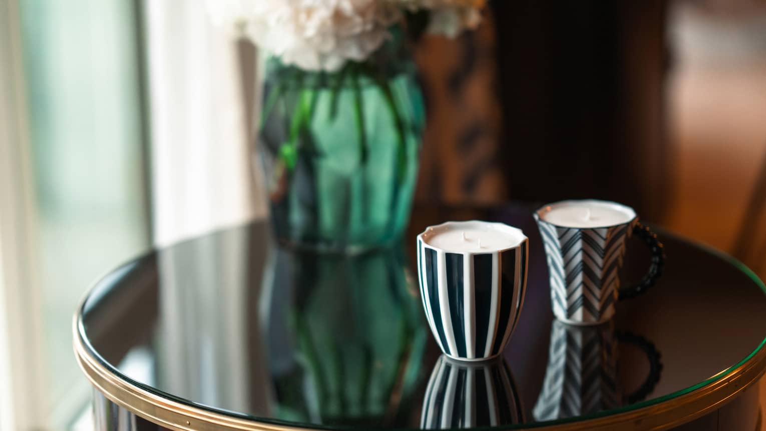 Two black-and-white ceramic candles set on round black table with green vase in backdrop