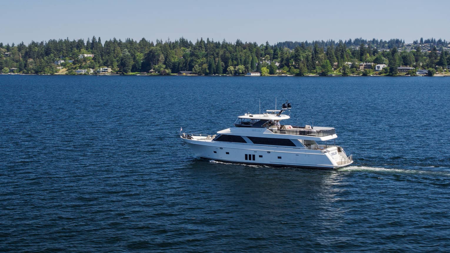 A yacht on water with a forest on the shore.