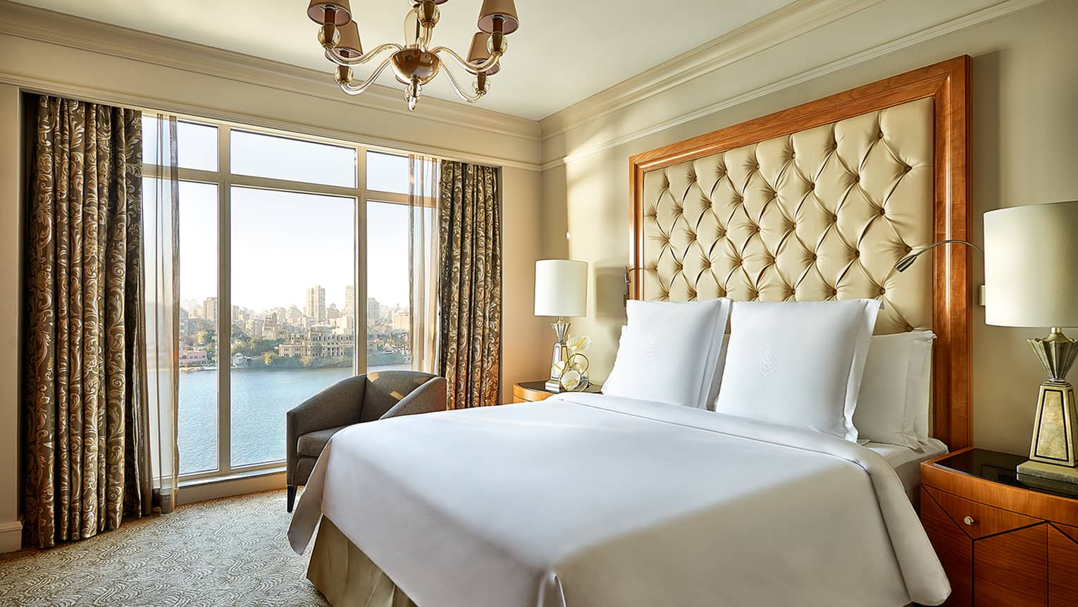 Diplomatic Suite bed with white bedspread, pillows and tall beige leather headboard beside tall window with river view