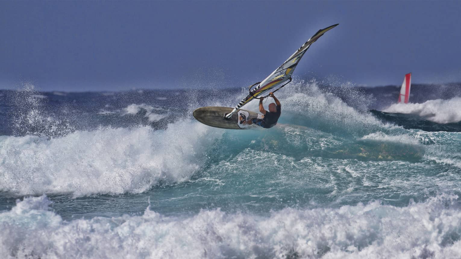Man windsurfs over crashing wave on ocean