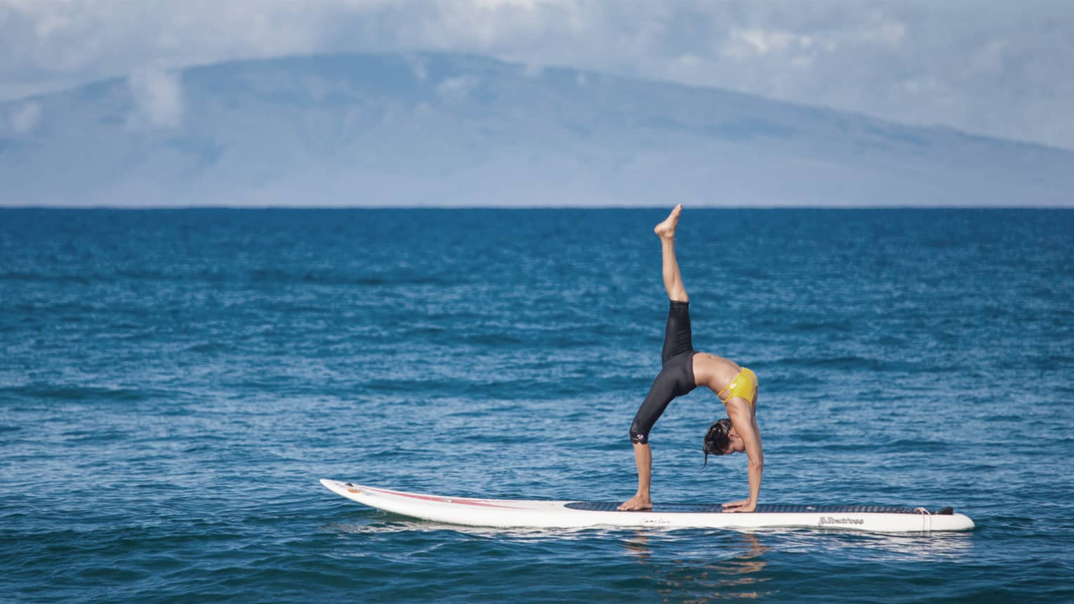 Woman balances in upside-down yoga pose on paddleboard on ocean