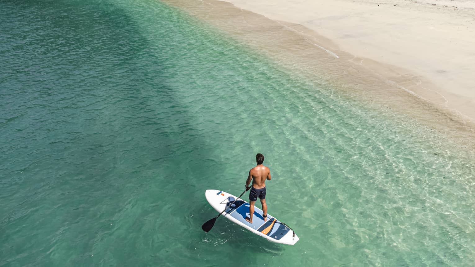 Aerial view of a man riding a stand-up paddleboard close to the shore