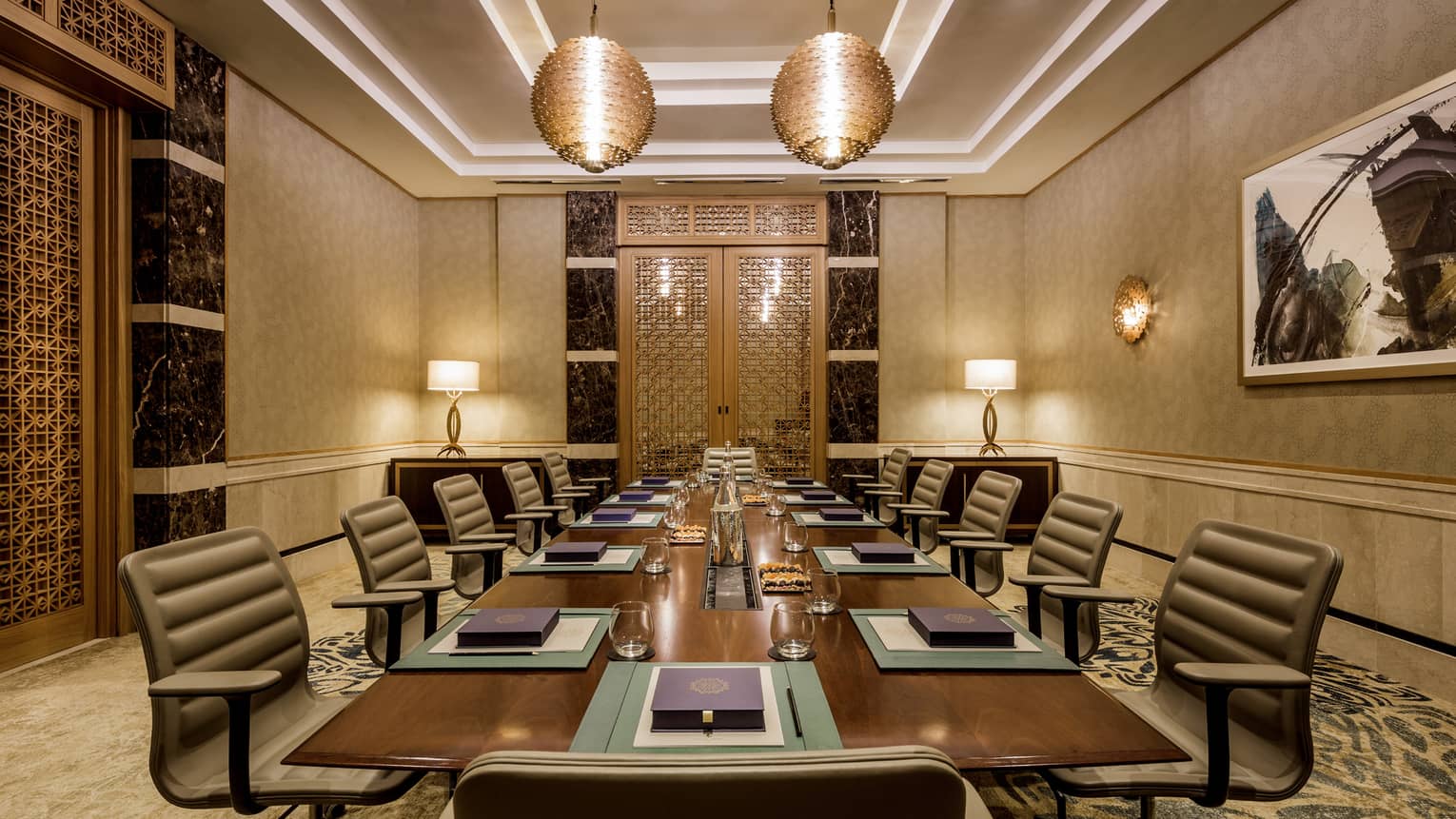 Executive table with large chairs in intimate boardroom accented with gold, ornate lights 