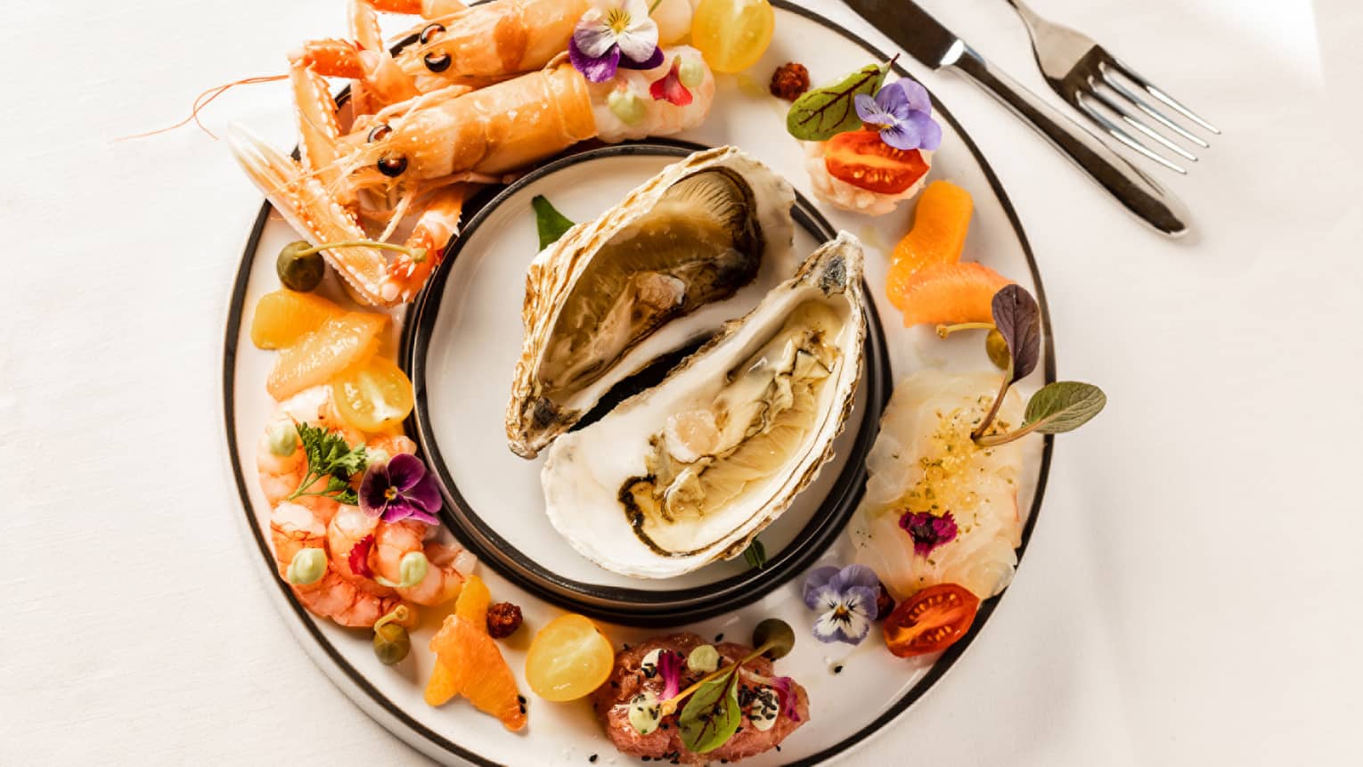 Selection of raw fish and shellfish on round plate with two in-shell raw oysters in centre