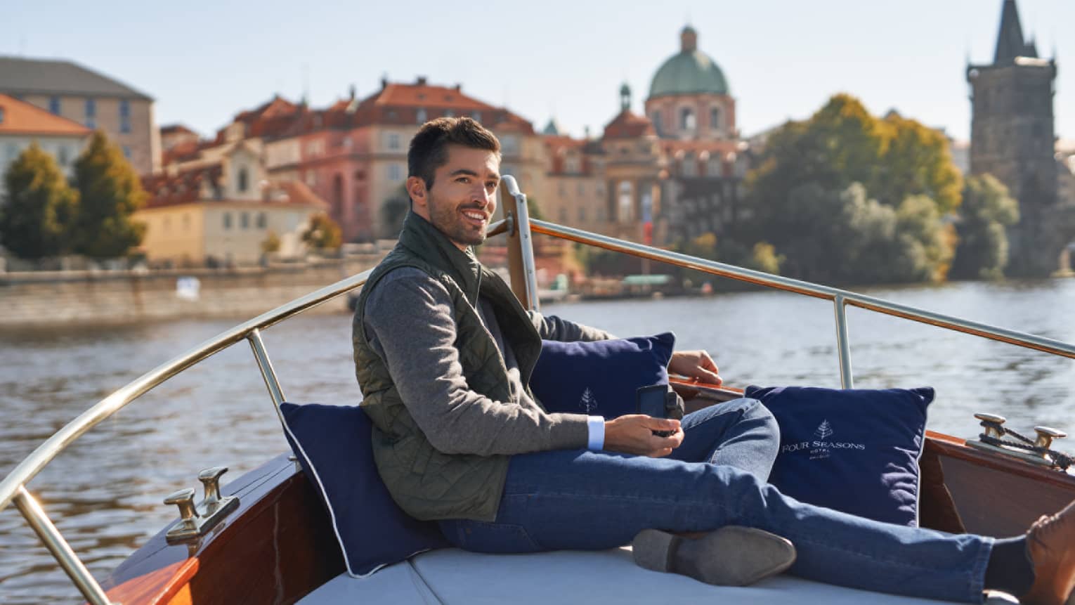 A man sits at front of wooden boat on river in Prague