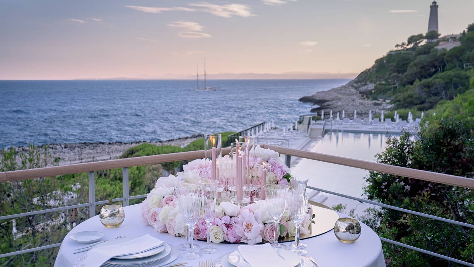 Balcony with round set table, pink floral arrangement, water views at sunset