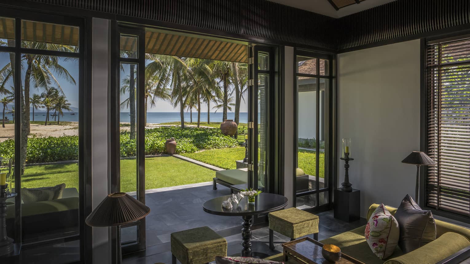 Ocean-Villa living room with open walls to patio, green lawn, tall palm trees