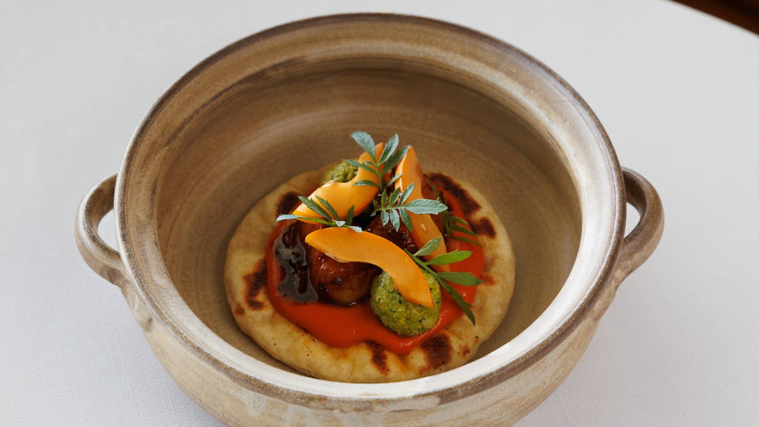 Lobster Topped with Romesco Sauce, Chickpea, Apricot and Tagete in tan ceramic crock on white table