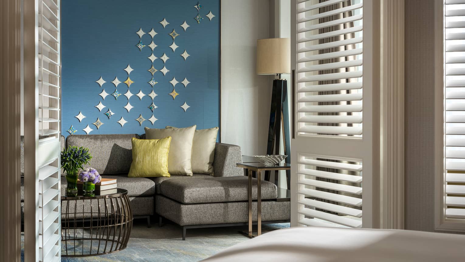 Gold pillows on grey sofa against blue wall with star-shaped Peranakan tile mural